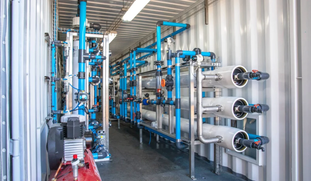 Interior View Of A Containerized Water Treatment Plant With Blue Tanks And Piping, Providing A Reliable Water Source For Food Production.