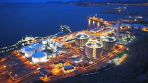Aerial Night View Of A Large Coastal Industrial Complex With Illuminated Storage Tanks And Processing Facilities, Highlighting The Scale Of Water Usage In Industry.